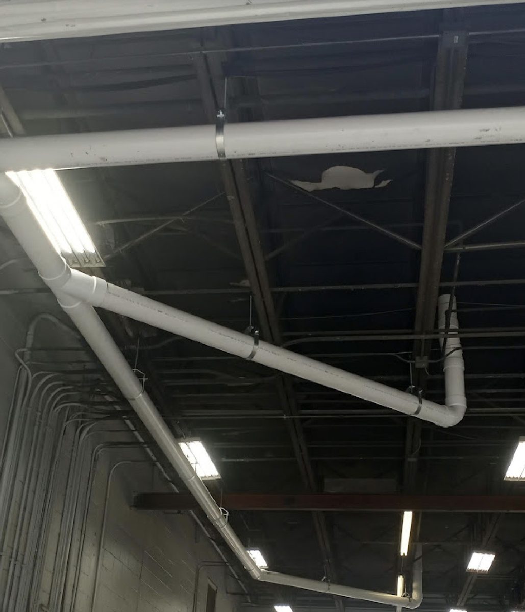 Six-inch roof leader running diagonally across the roof trusses of a commercial maintenance building