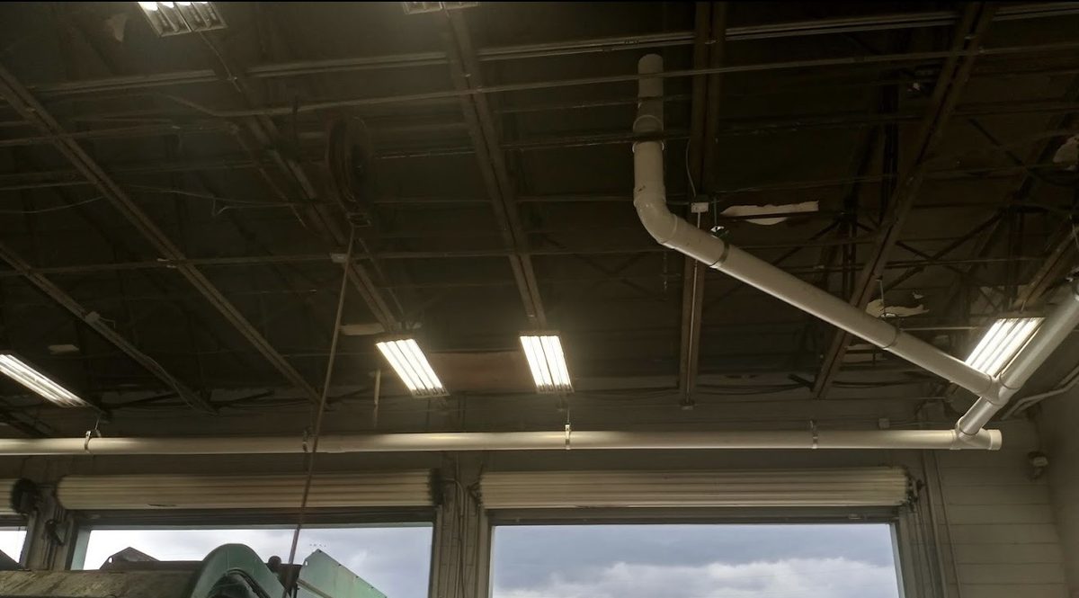 Six-inch PVC commercial roof leader running along the header above the bay doors of a fleet maintenance building